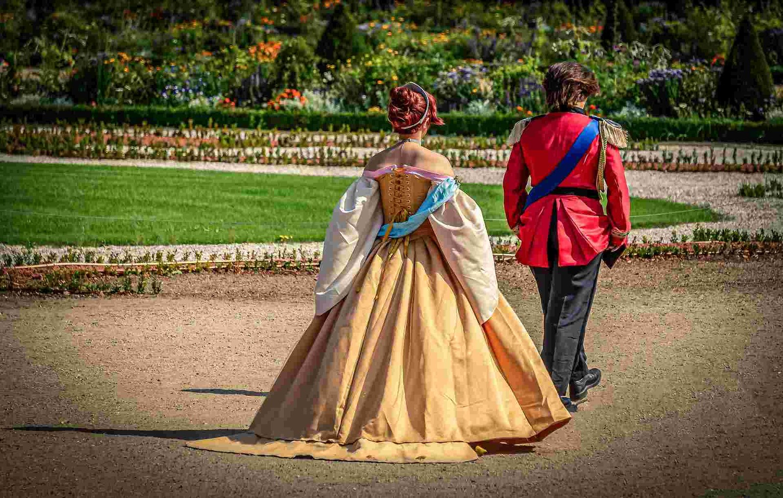 Princes-in-victorian-golden-dress-walks-behind-a-prince-in-army-uniform-in-a-garden